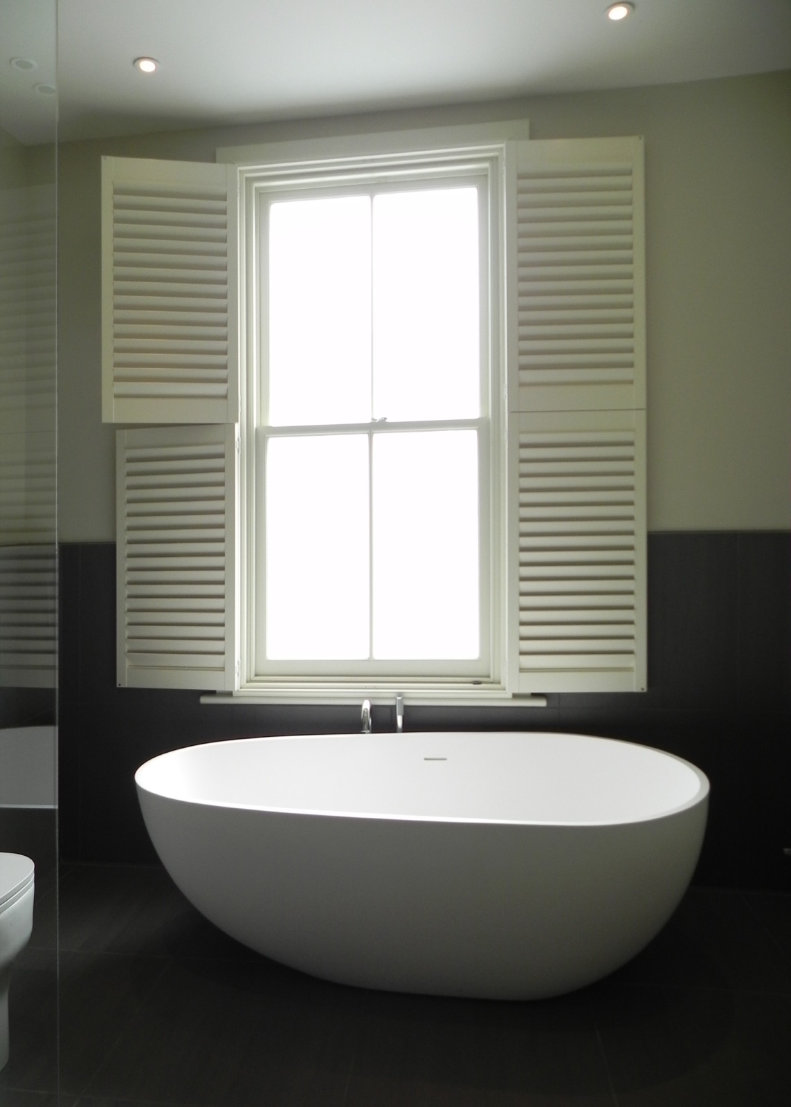 Bathroom with a freestanding bath beneath a shuttered sash window