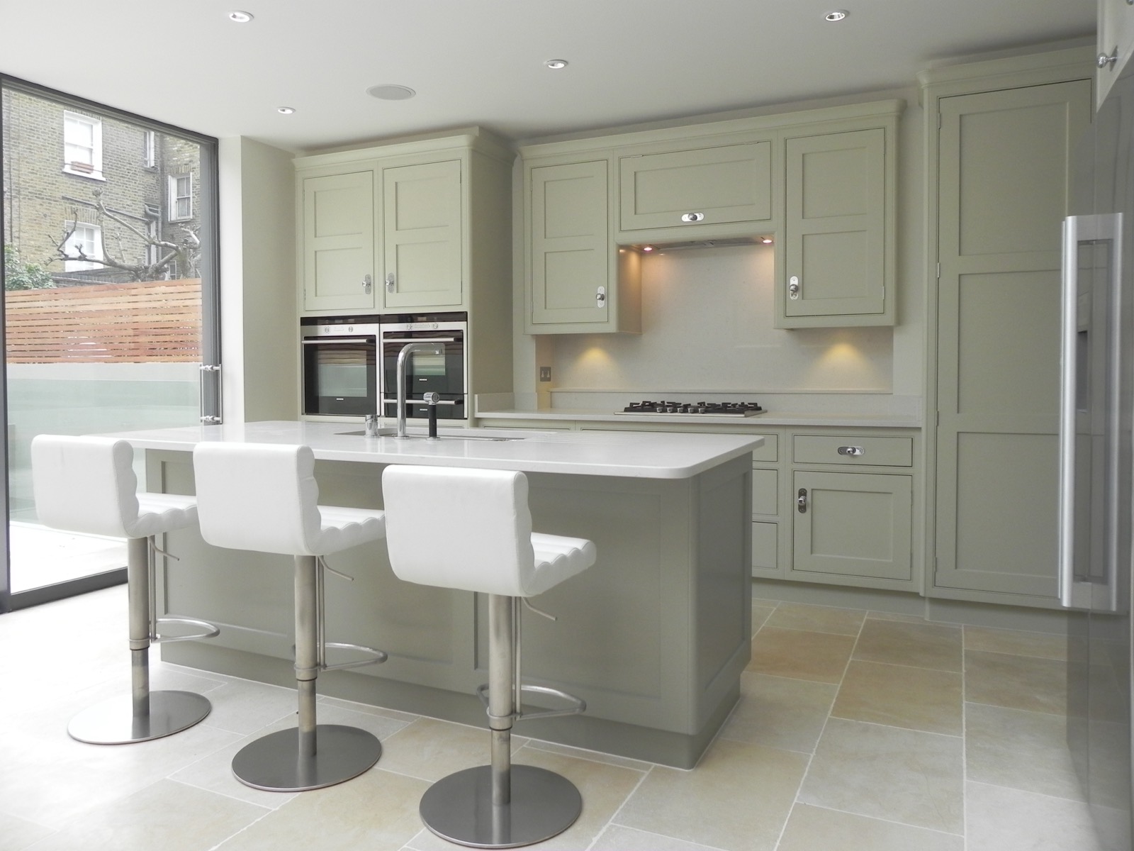 Sage green kitchen with an island beside garden glazing