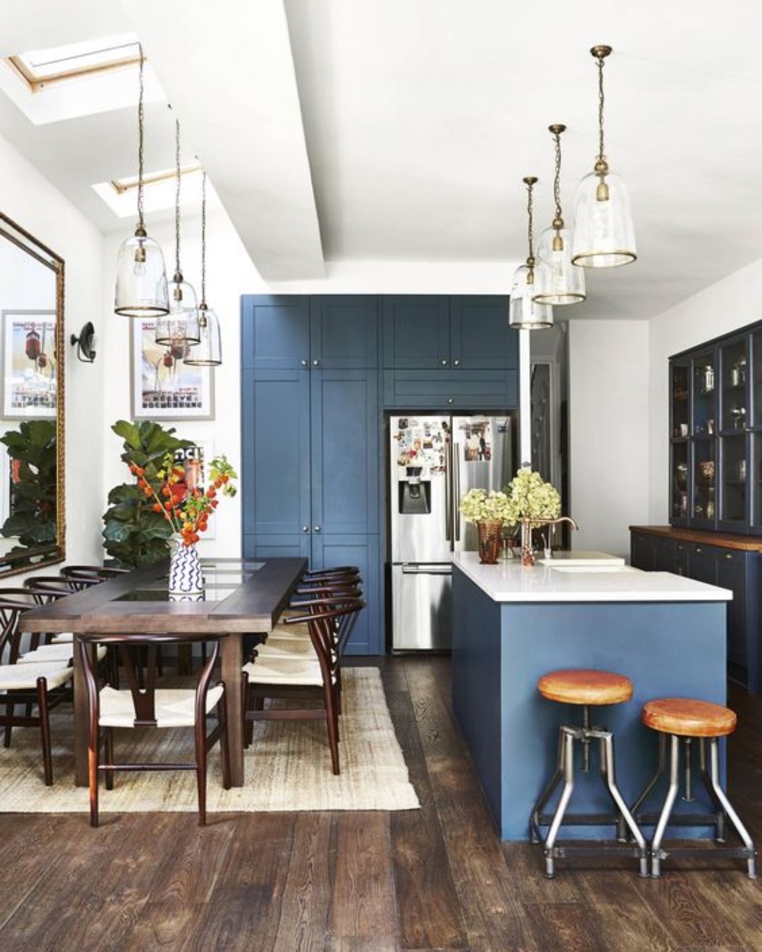 Blue kitchen with an island, pendant lights and a dining table on a dark timber floor