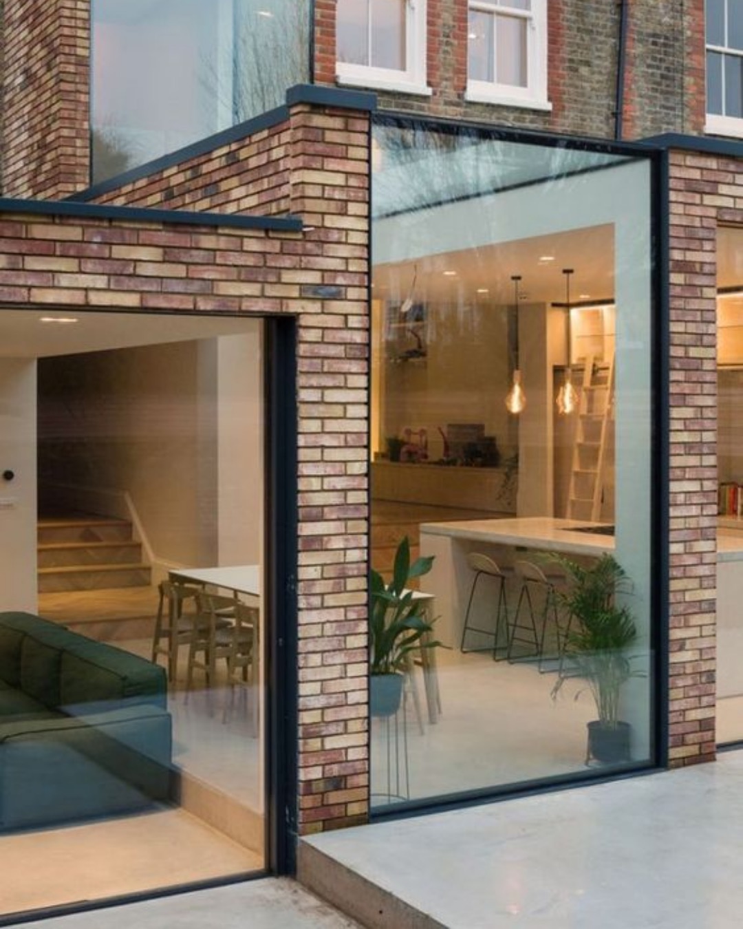 Brick and glass corner of a kitchen extension lit at dusk