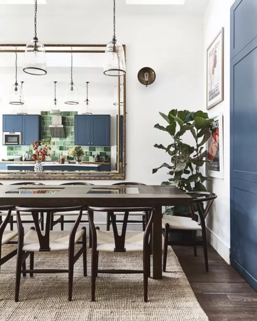 Long dining table with pendant lights and a large mirror reflecting a blue kitchen
