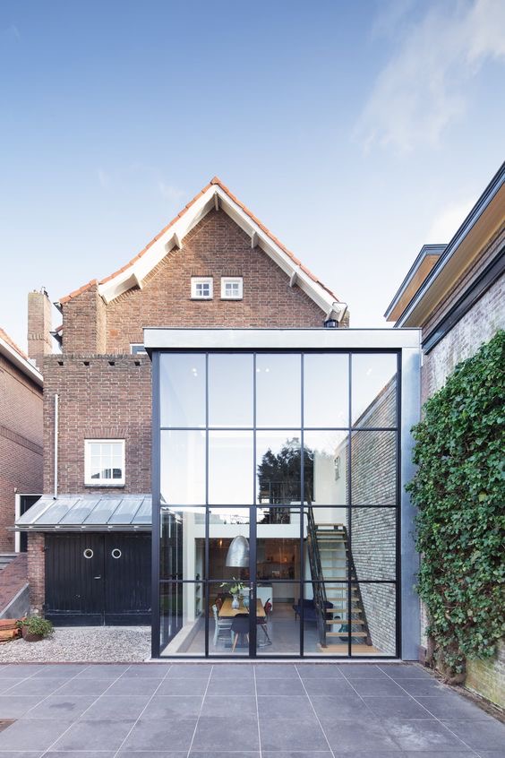 Double-height steel-framed glazed extension on a brick house with a tiled gable