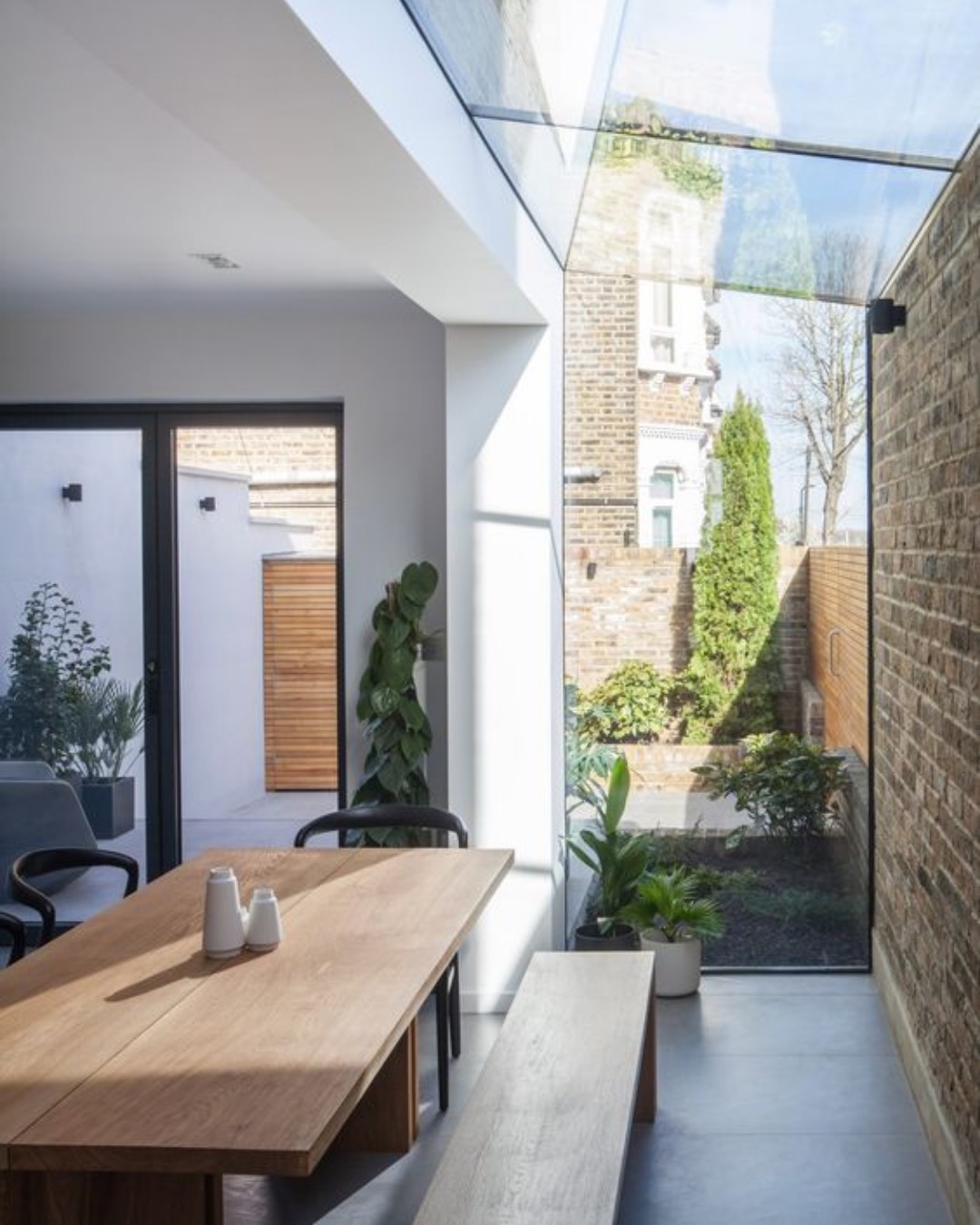 Dining table beside a frameless glass infill looking onto a small garden