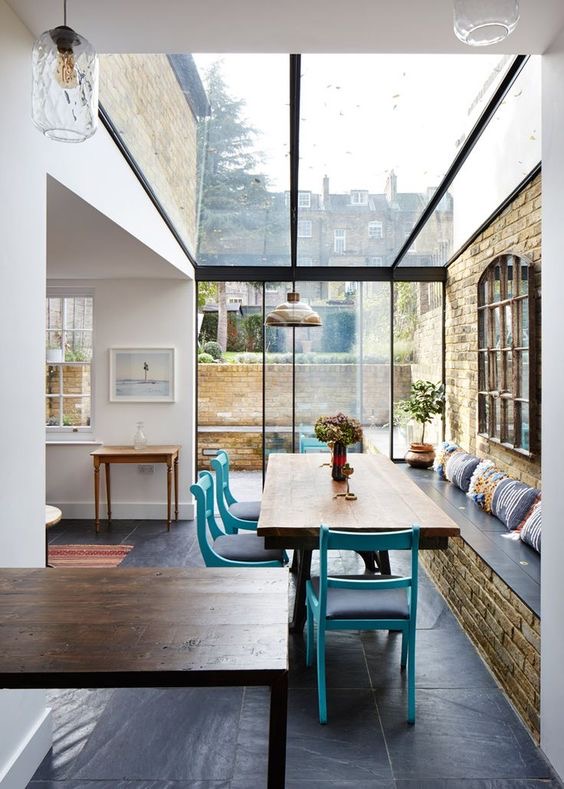 Dining area in a glass box extension with a slate floor and an exposed brick wall