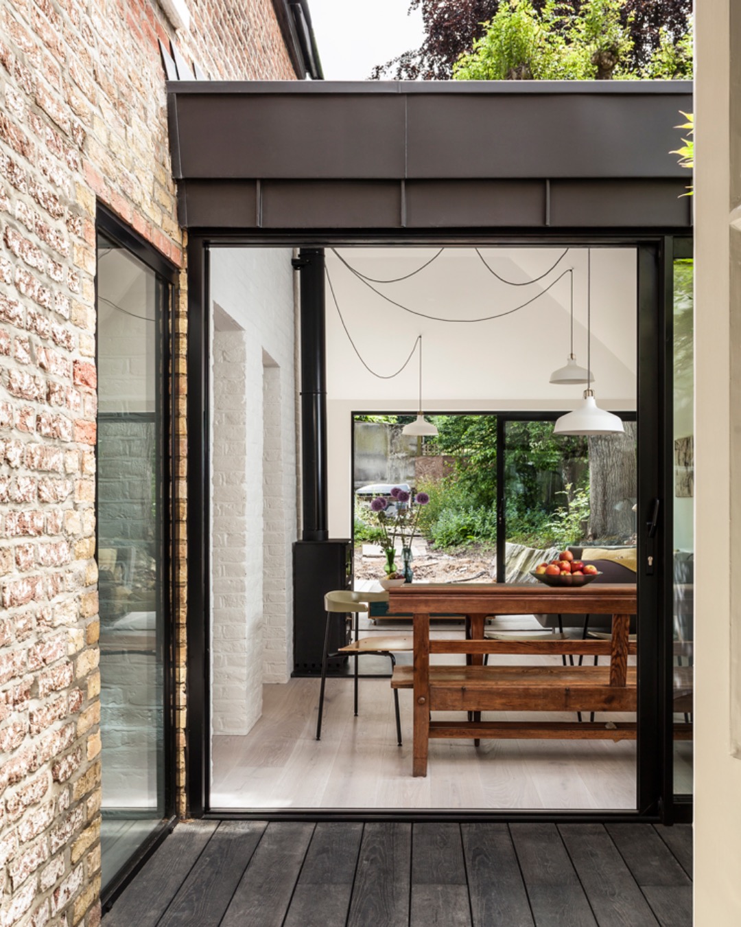 Glazed garden room with a dark metal roof between brick walls, with a dining table inside