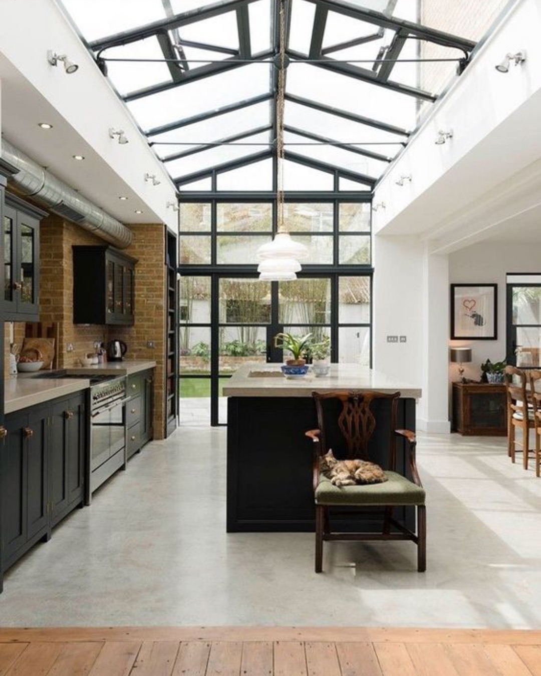 Kitchen under a pitched glazed roof with steel-framed doors, exposed brick and dark cabinets
