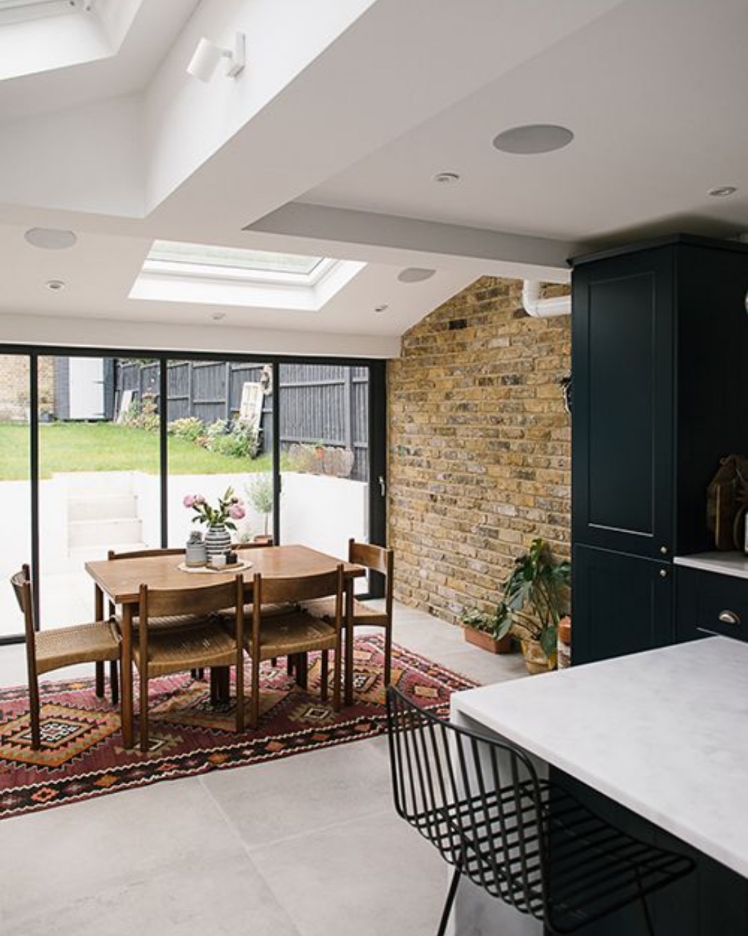 Dining area in a flat-roofed extension with a rooflight, sliding doors and an exposed brick wall