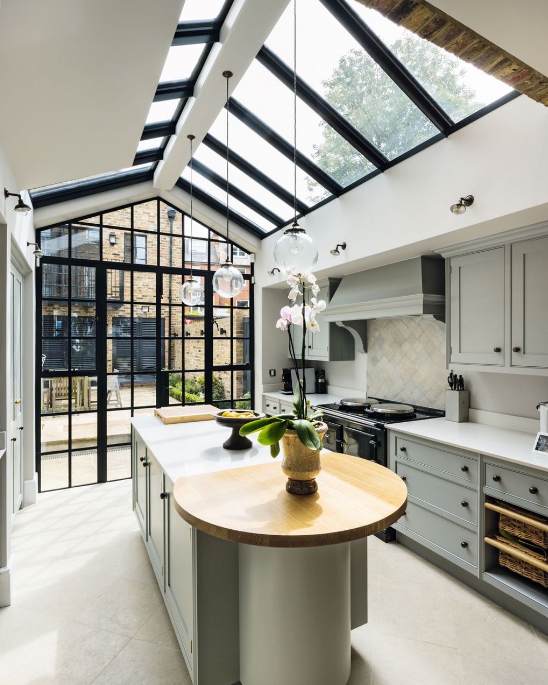 Kitchen with sage green cabinets under a glazed pitched roof and a steel-framed gable window