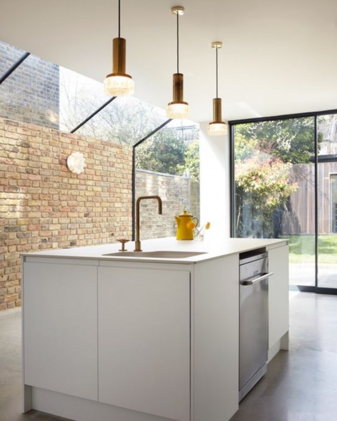 Kitchen island beside a frameless glass side return with an exposed London stock brick wall